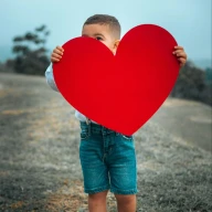 Chłopiec trzymający wycięte duże czerwone serce
